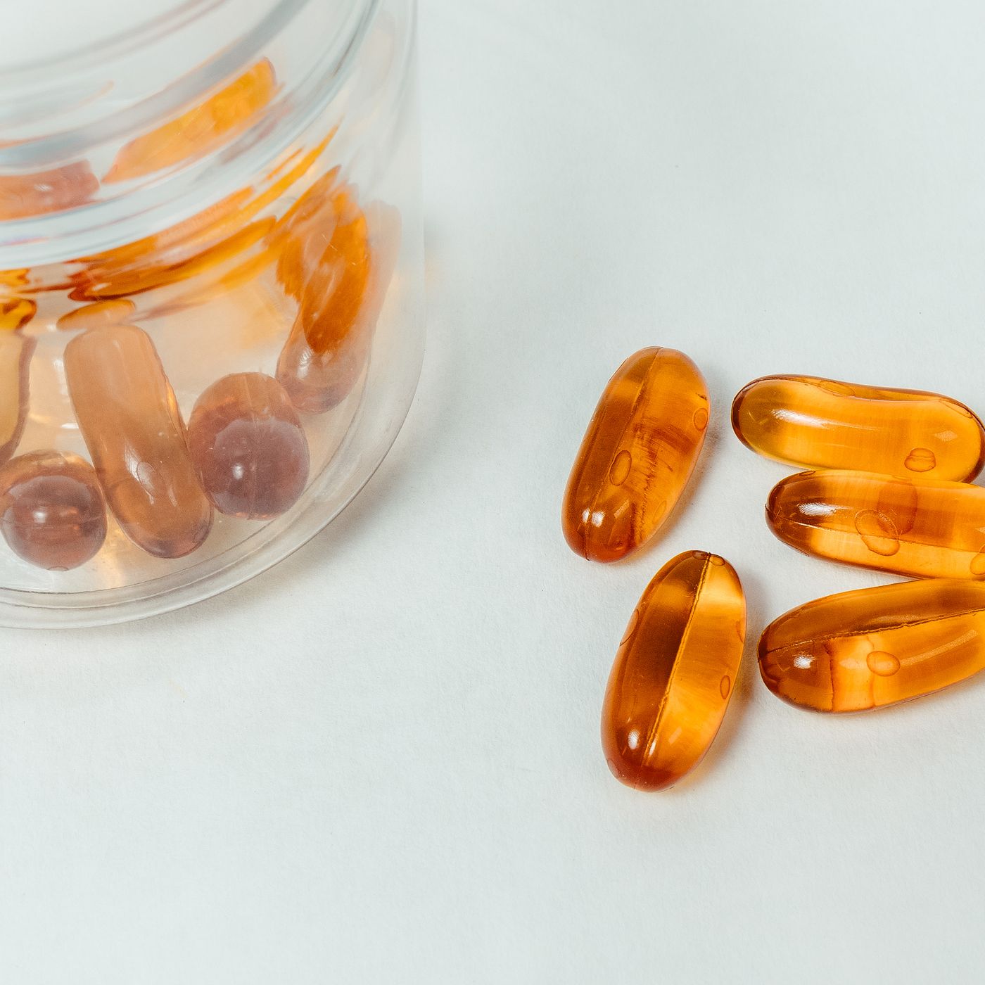Amber softgel capsules beside a clear glass jar