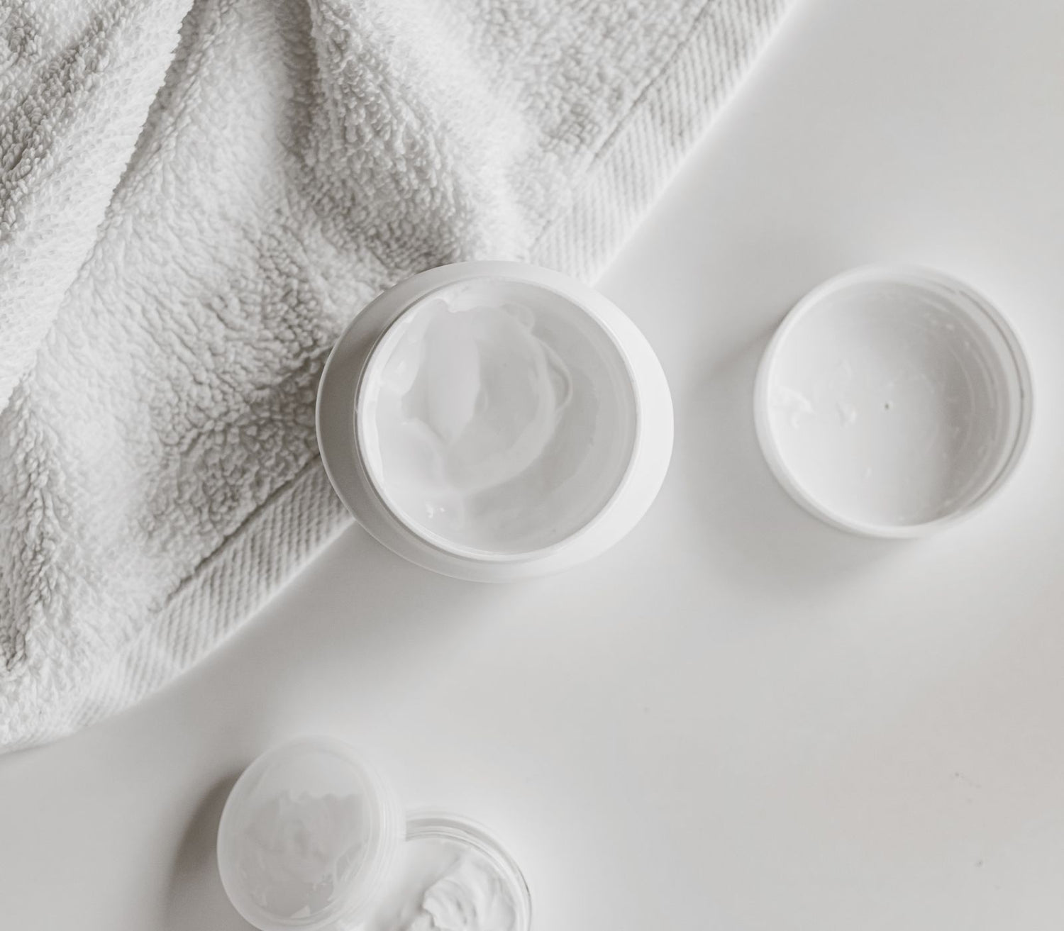 Open jars of unfragranced cream on a white towel