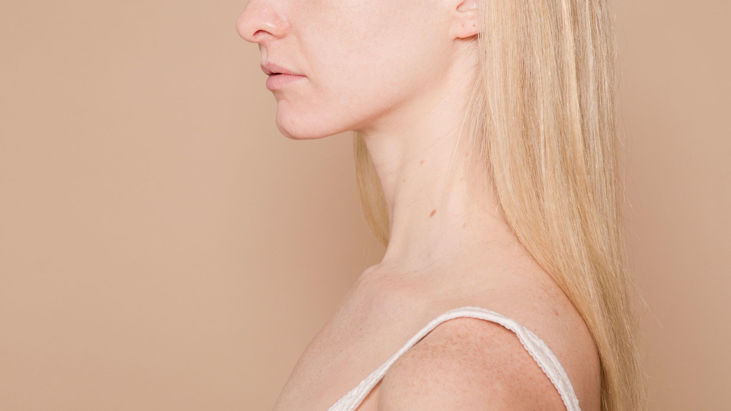 Side profile of a woman with clear, bare skin against a pale neutral background